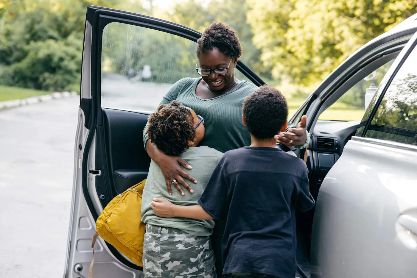 Woman with two kids standing by open car door.