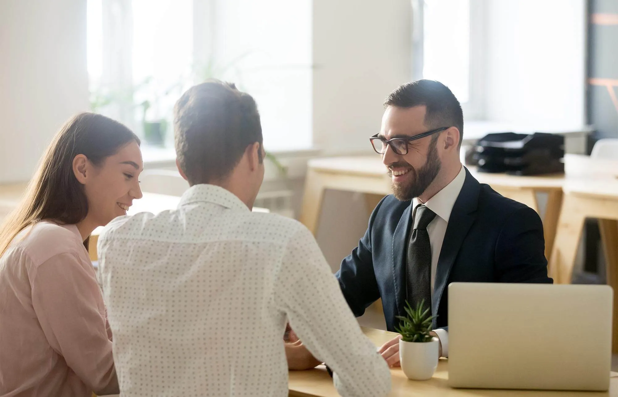 A man in a suit talks to a couple from across the table.