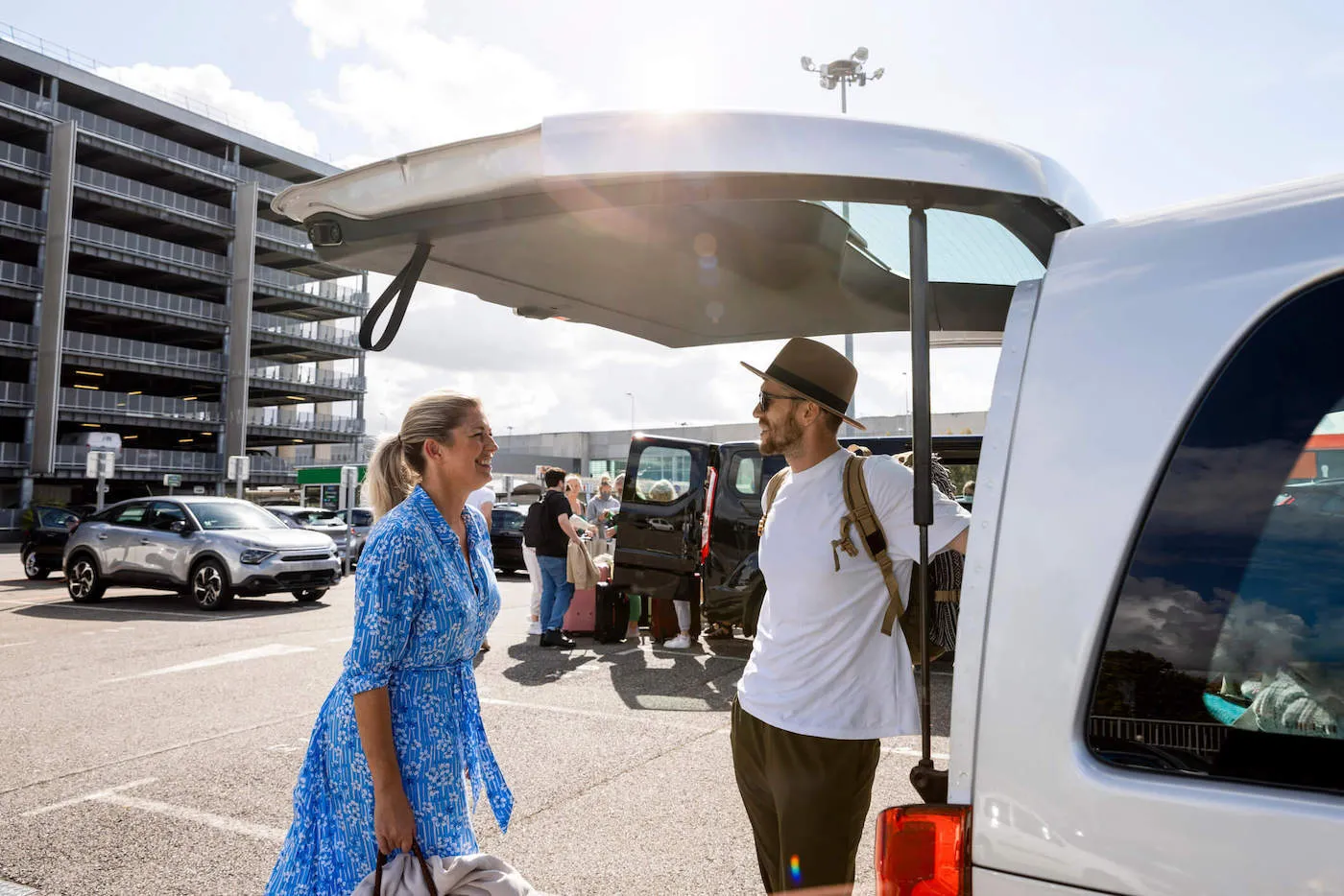 Young man and woman couple on vacation standing beside open car trunk in rental car lot.