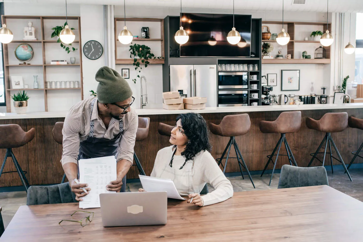 Young man and woman in aprons working with a pile of papers on an open table.