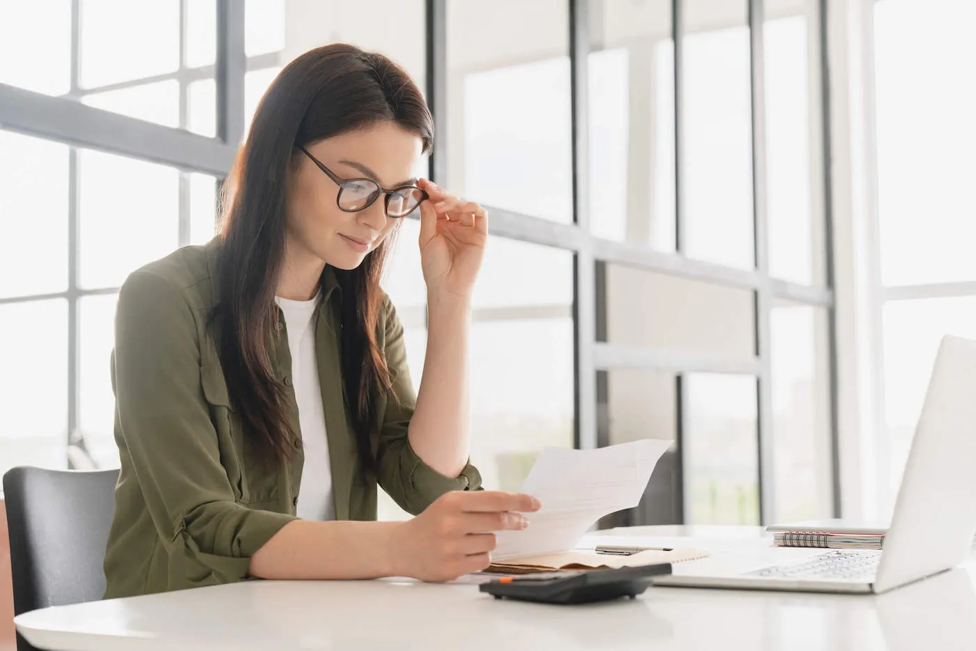 Young woman holding glasses while looking at a statement balance paper.