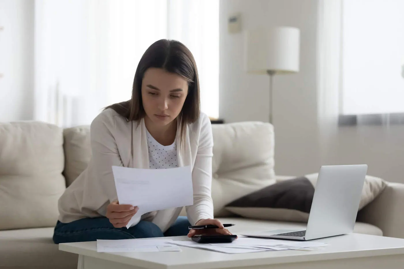 Young woman looking at paper while seated on a sofa in the living room.