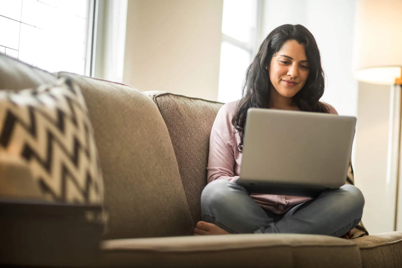 Young woman seated cross-legged on a sofa researching buy now pay later on laptop.