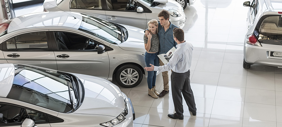 Car dealer showing new car to young couple in showroom