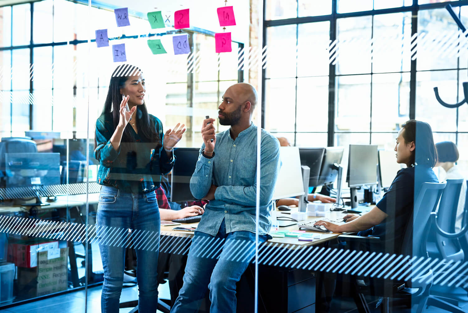 Male and female co-workers discussing in front of a glass wall office with stickies attached ot the wall.